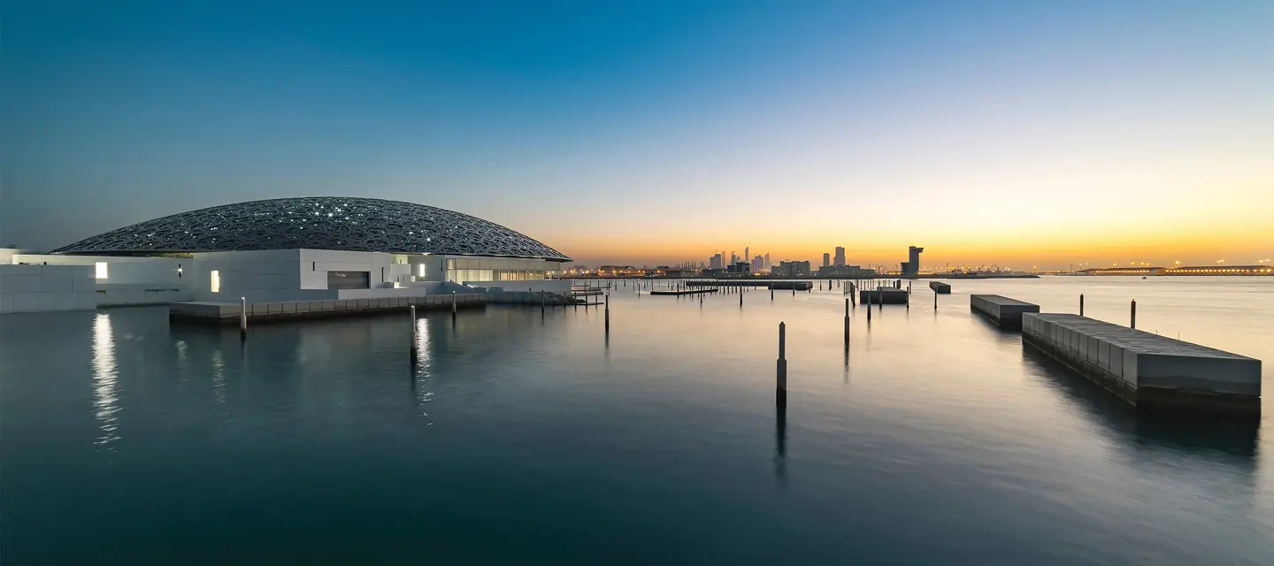 Louvre Abu Dhabi dome beside calm waterfront at sunset