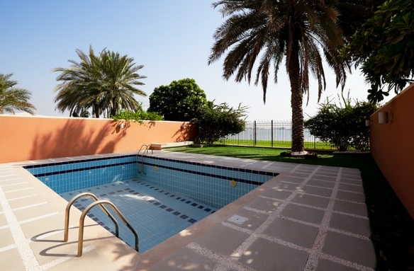 Empty private swimming pool beside a palm-lined garden at a Mangrove Village villa in Abu Dhabi