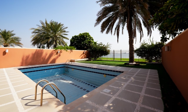 Empty private swimming pool beside a palm-lined garden at a Mangrove Village villa in Abu Dhabi